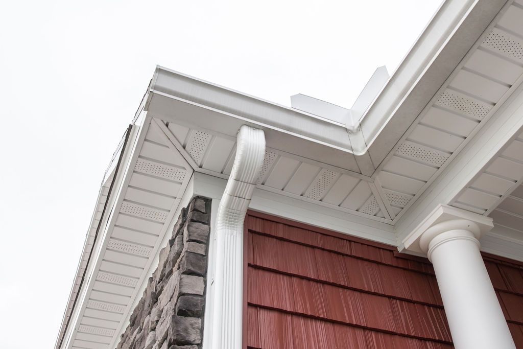 The corner of a house with a white gutter and a red siding.