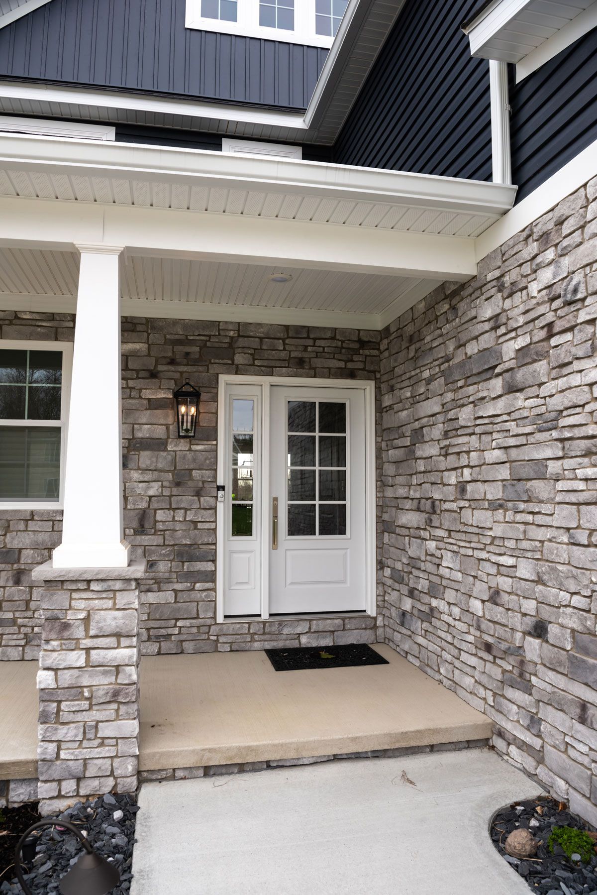 The front porch of a house with a stone wall and a white door.