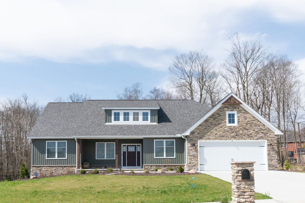 A house with a gray roof and a white garage door is sitting on top of a lush green hillside.
