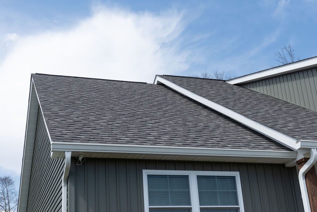 The roof of a house with a gray siding and a white trim.