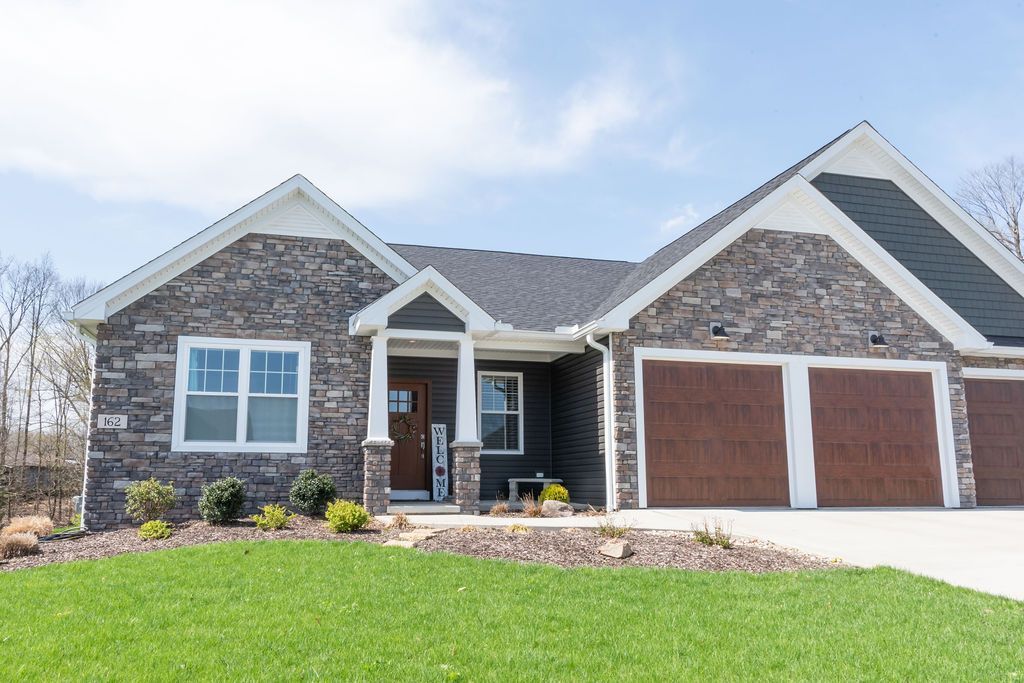 A large brick house with two garage doors and a lush green lawn in front of it.