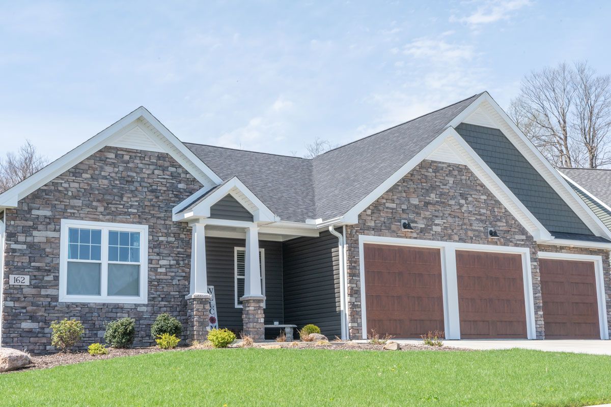 A large stone house with two garage doors and a lush green lawn in front of it.