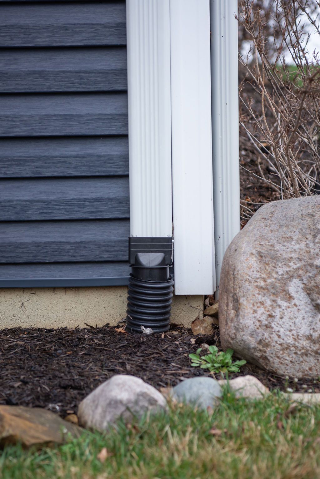 A drain pipe is connected to the side of a house next to a rock.