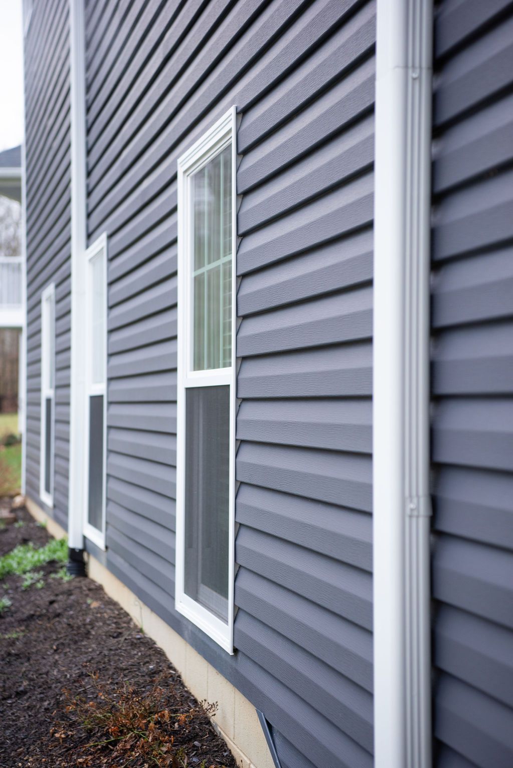 The side of a house with a gray siding and white windows.