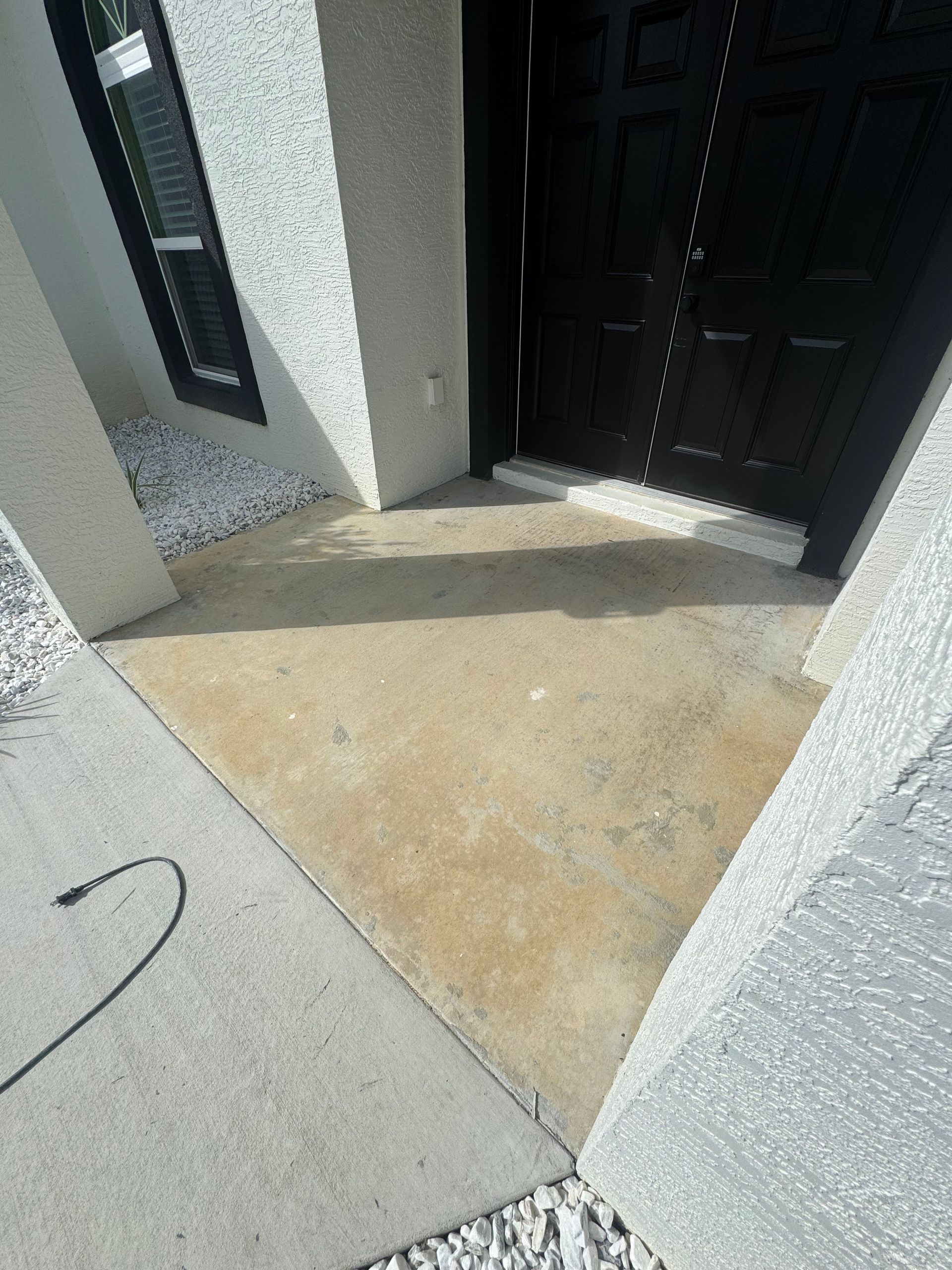 A concrete walkway leading to a black door of a house.