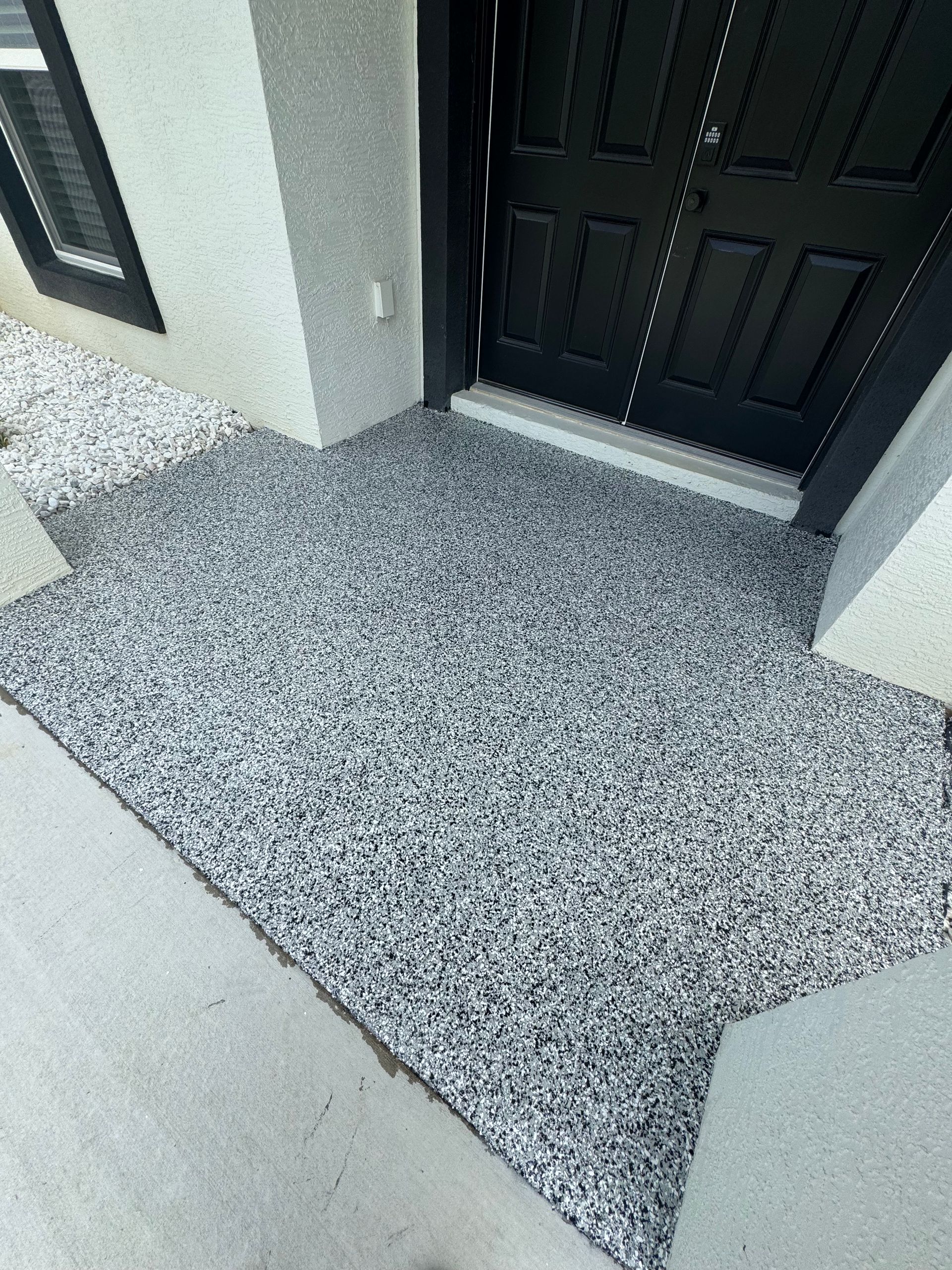 A concrete walkway leading to a black door of a house.