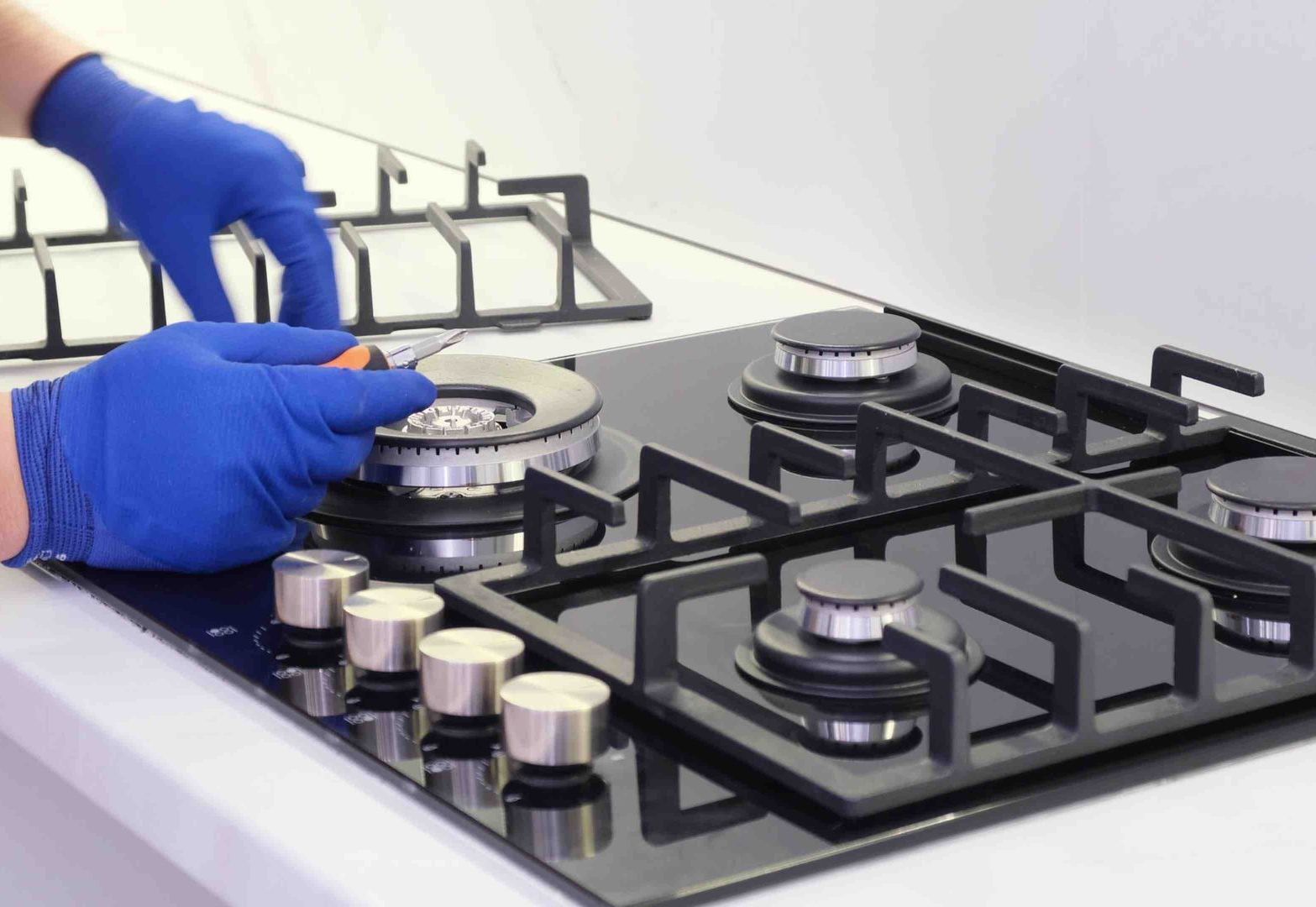 Gloved hands cleaning a stainless steel gas stovetop with silver control knobs