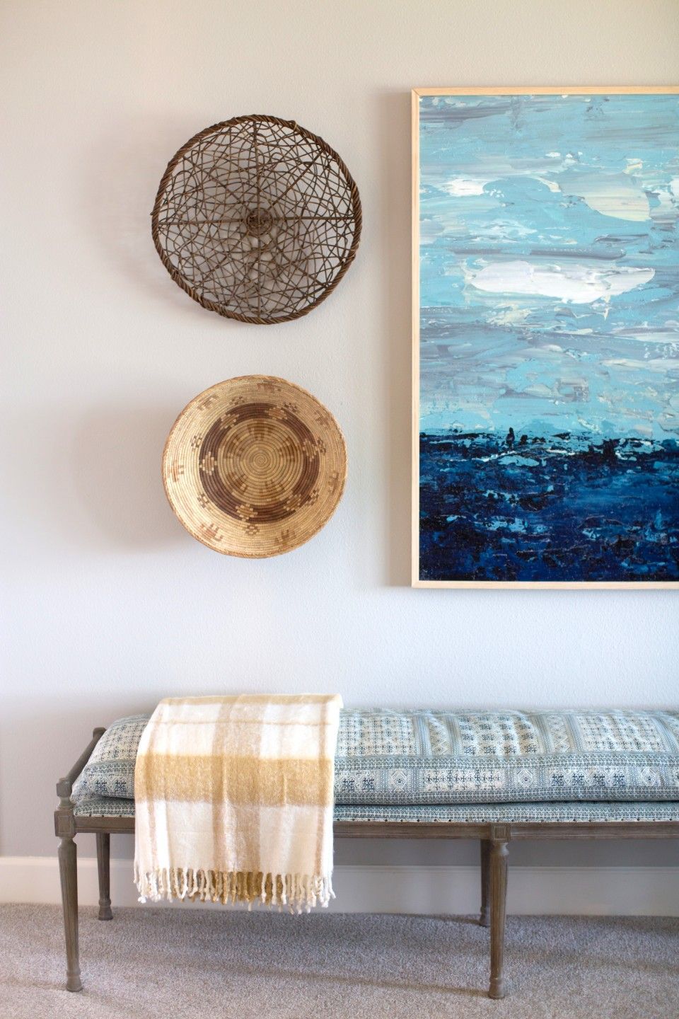 There is a painting on the wall above a bench with a blanket on it.