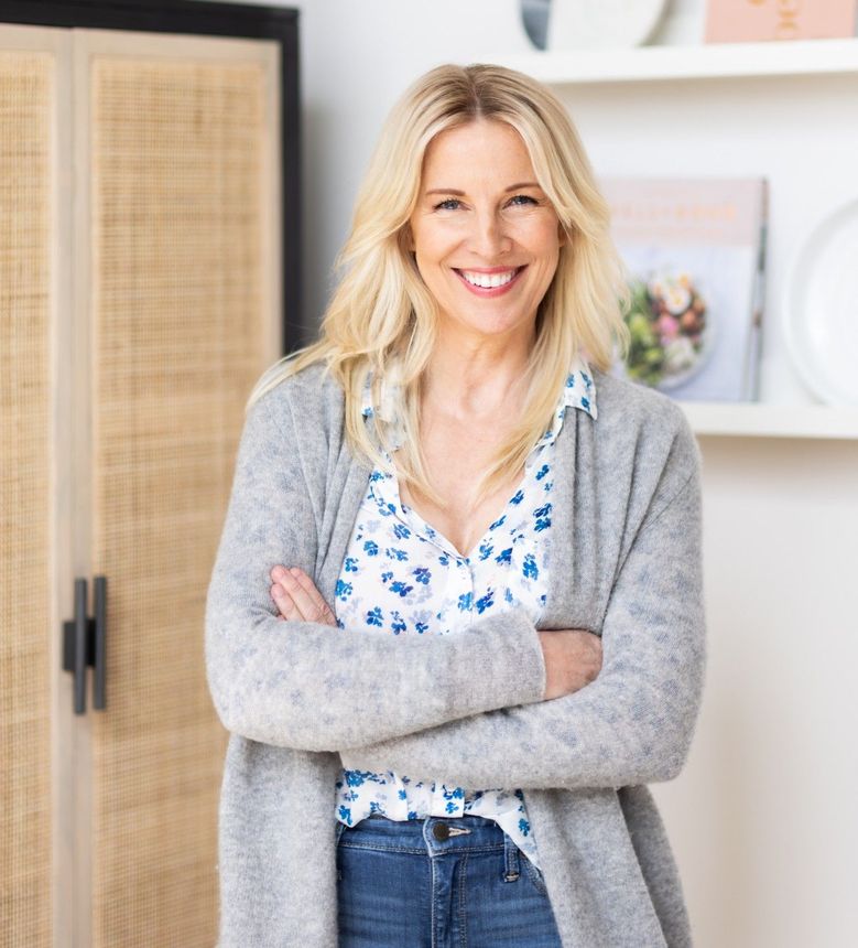 A woman is standing in a room with her arms crossed and smiling.