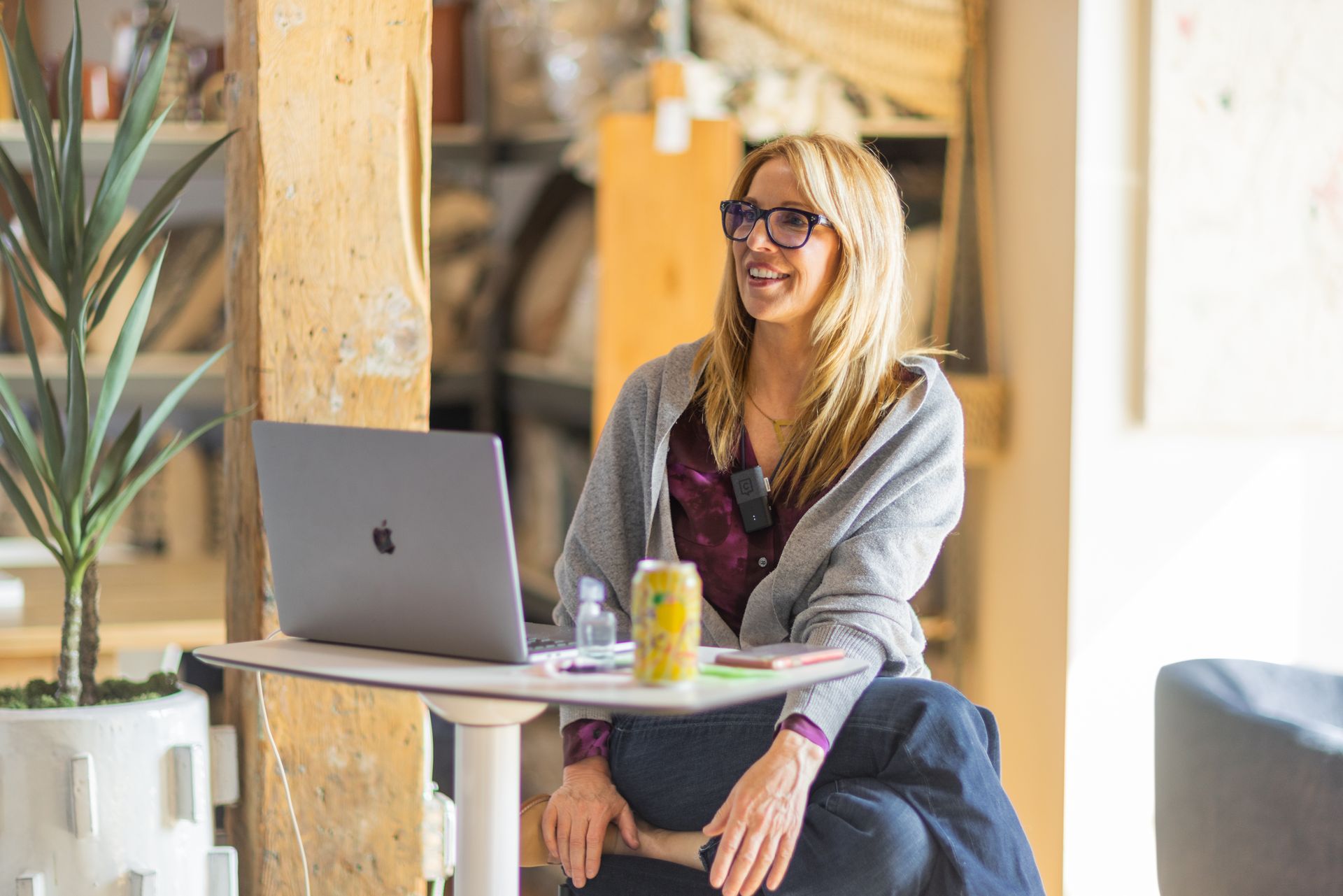 A woman is sitting at a table with a laptop and a can of soda.