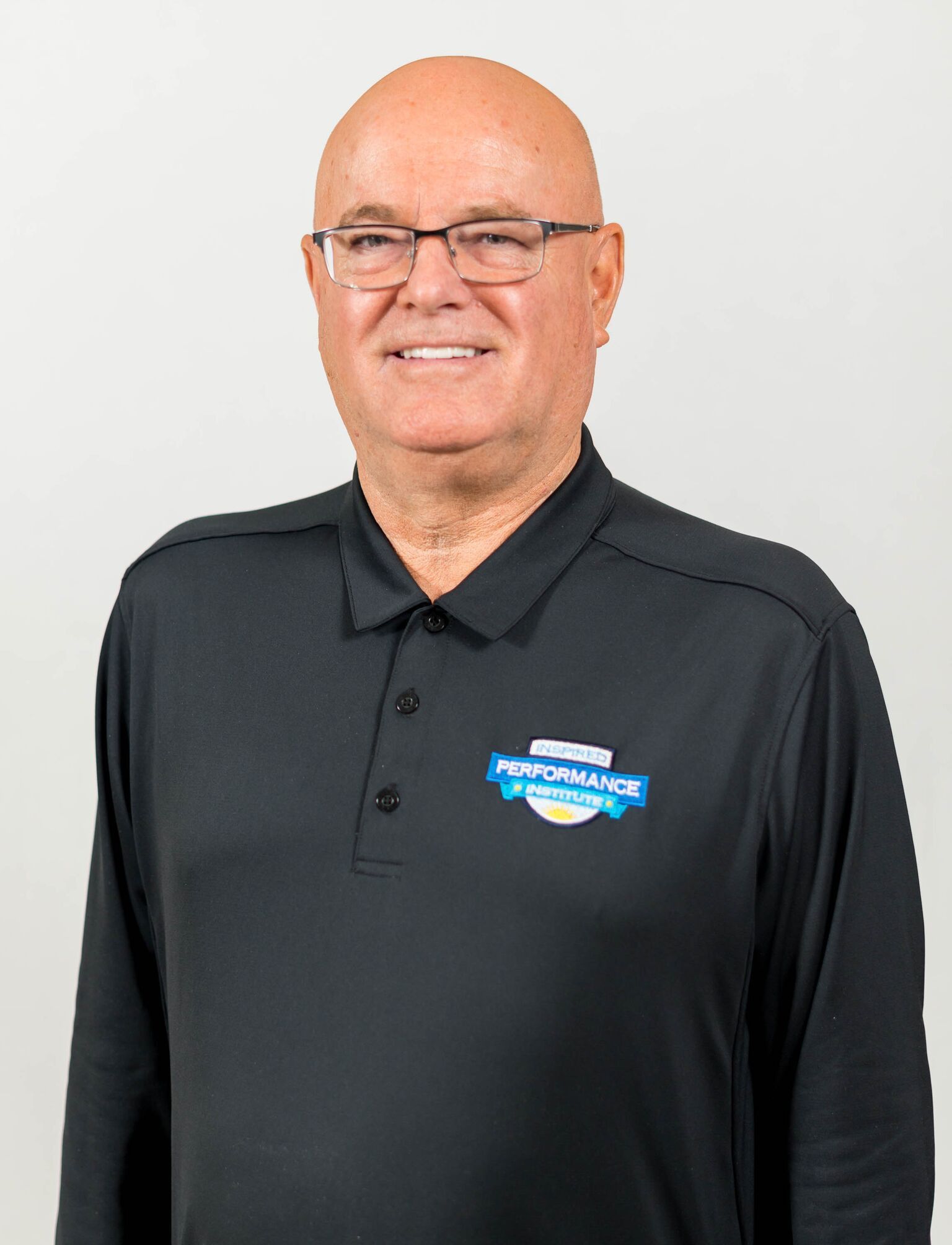 A bald man wearing glasses and a black polo shirt is smiling for the camera.