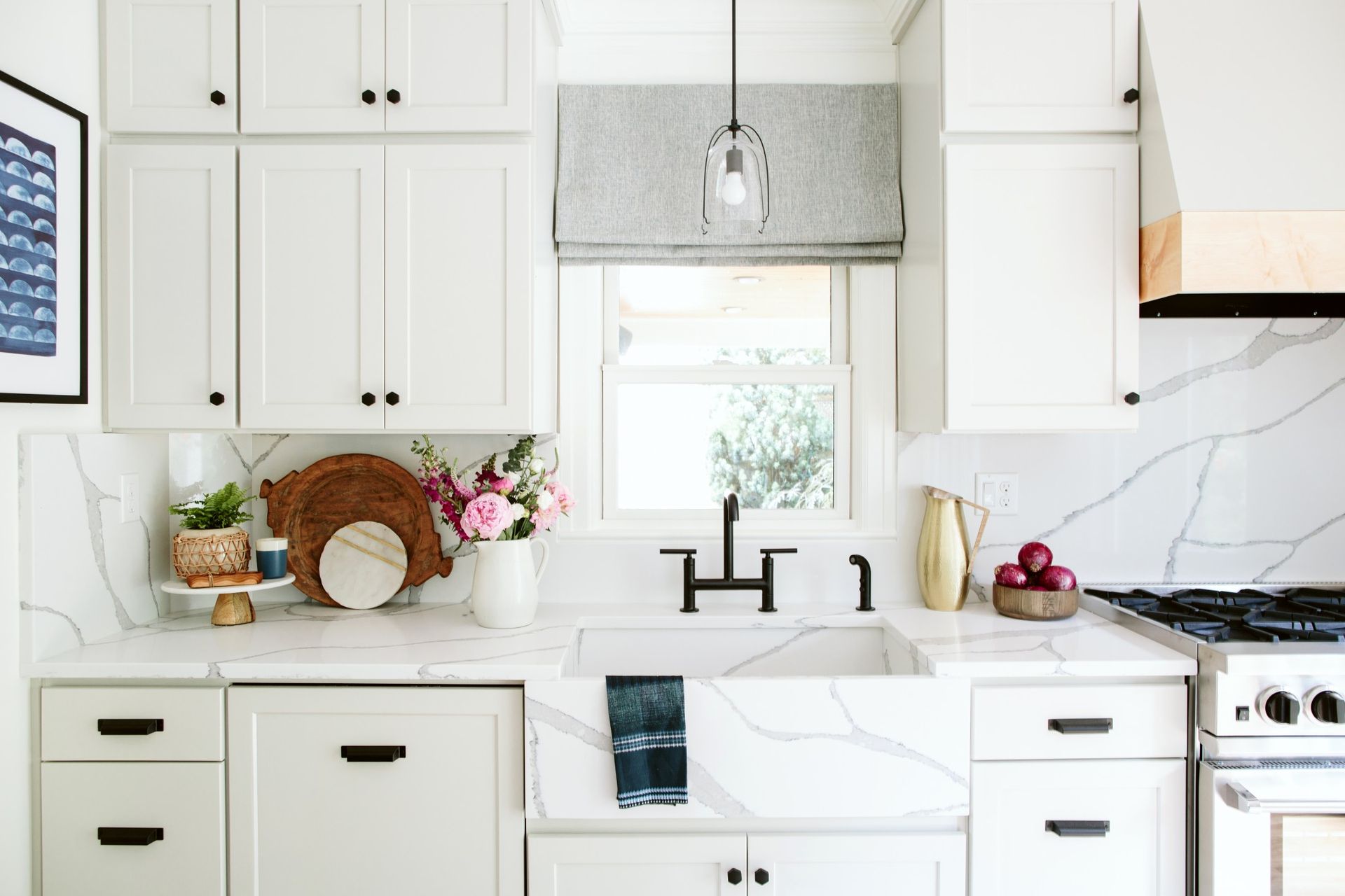 A kitchen with white cabinets , a sink , a stove , and a window.
