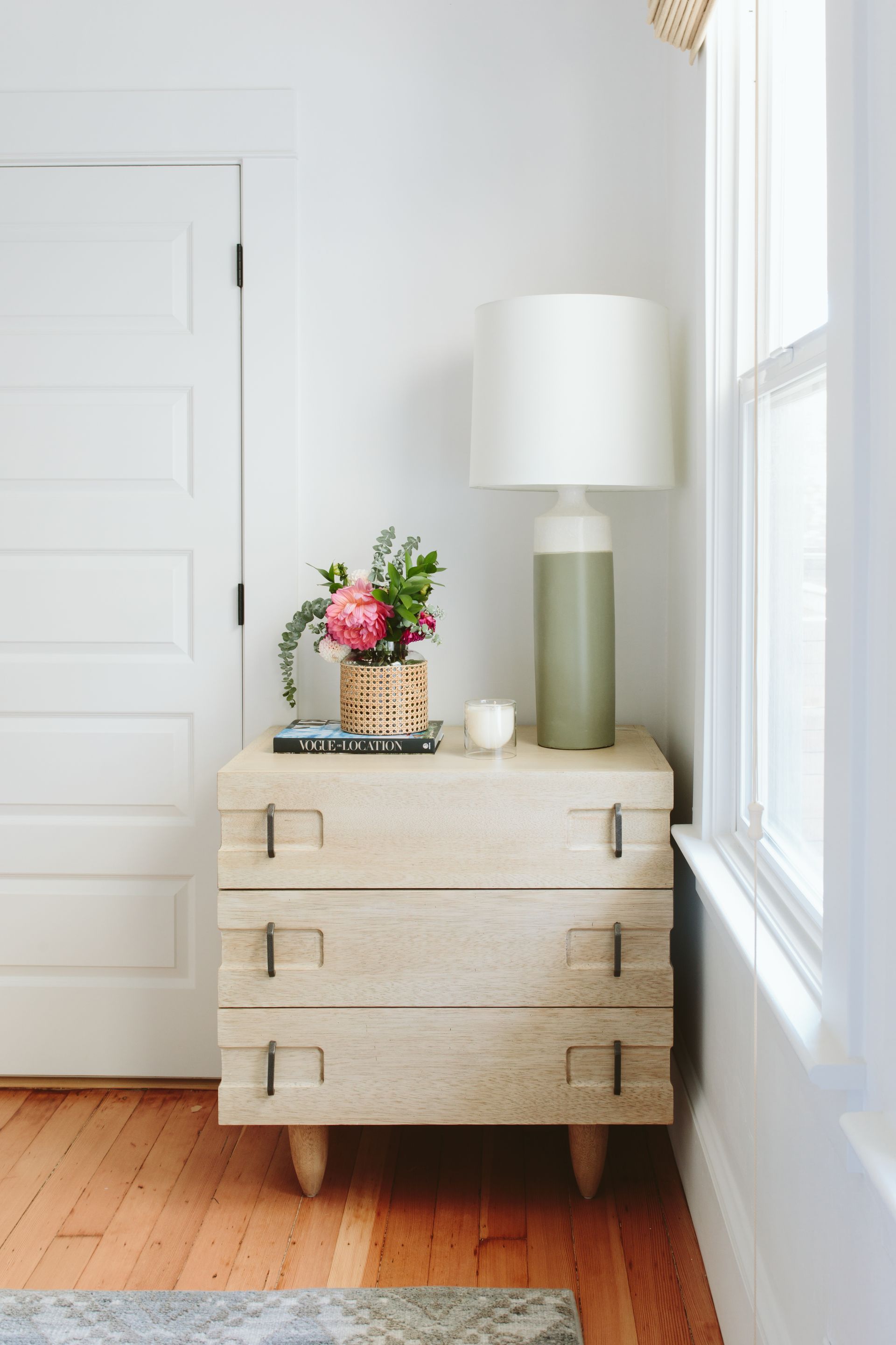 A dresser with a lamp and a vase of flowers on top of it.
