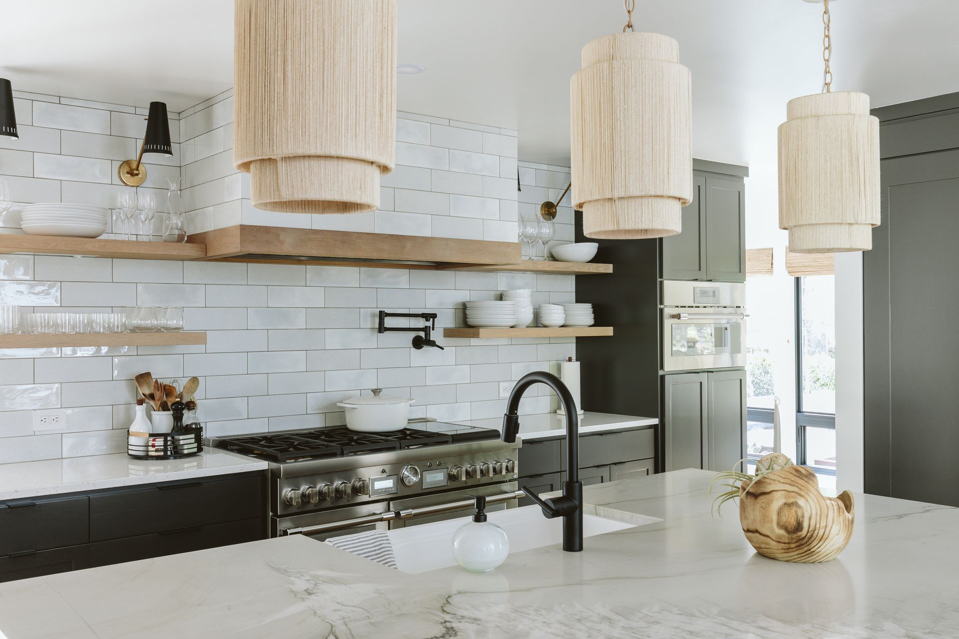 A kitchen with a stove , sink , and pendant lights.