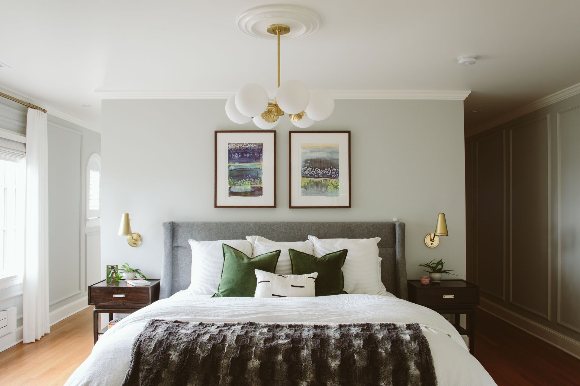 A bedroom with a bed , two nightstands , a chandelier and two pictures on the wall.