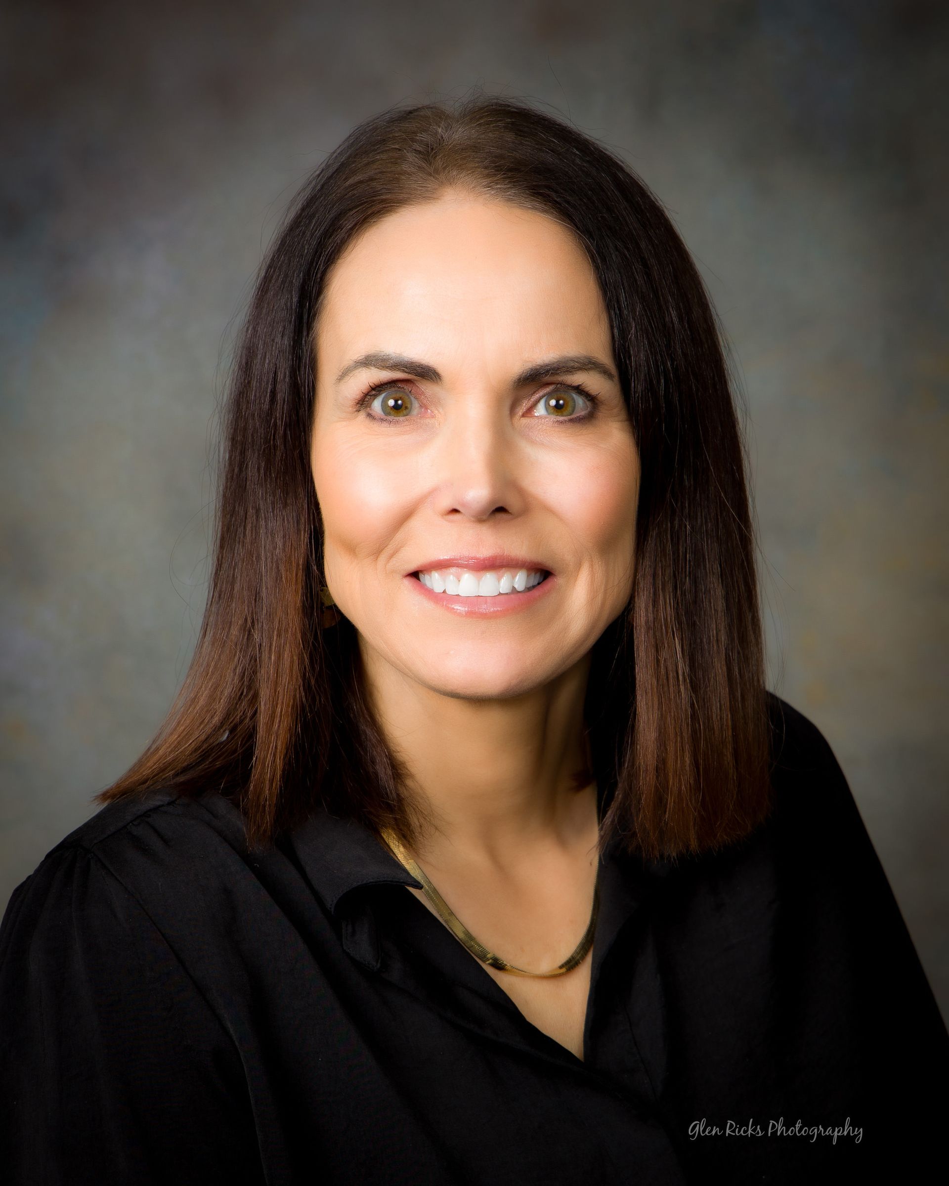 A woman wearing a black shirt and a gold necklace smiles for the camera
