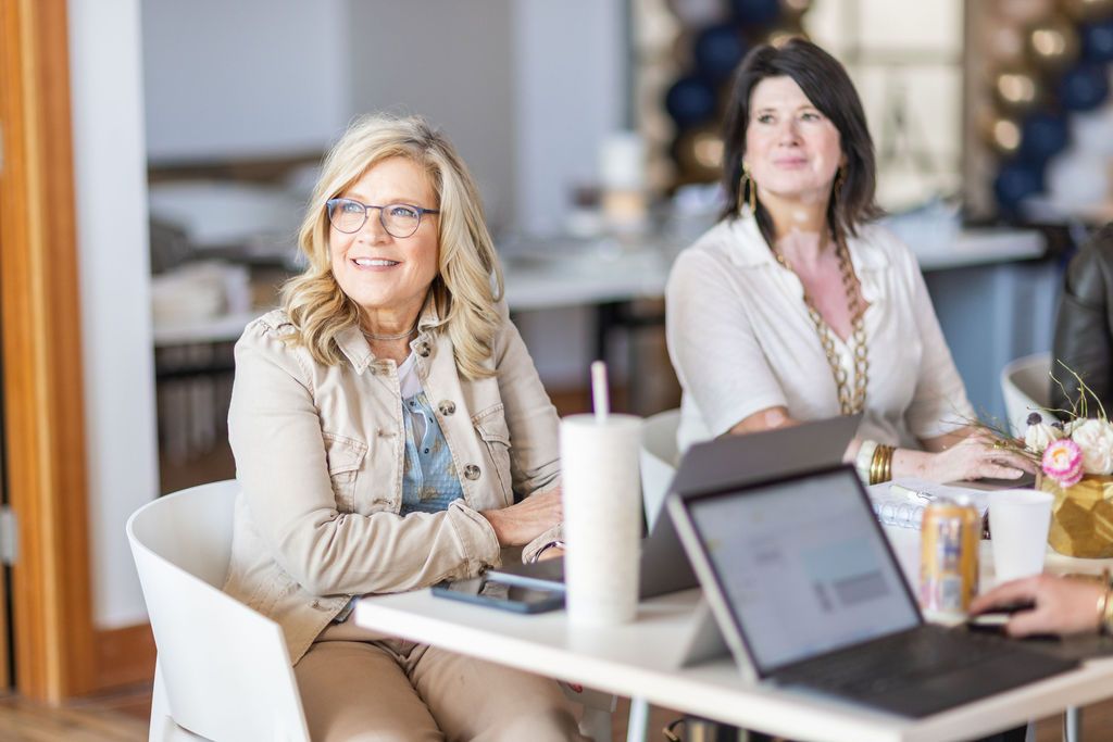 Two women are sitting at a table with laptops.