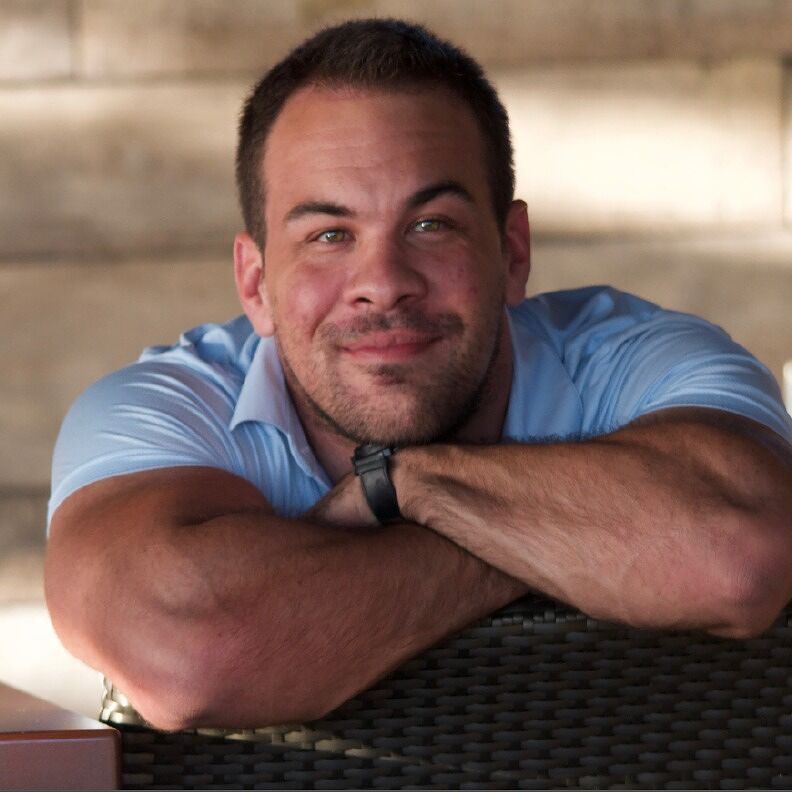 A man in a blue shirt is smiling with his arms crossed