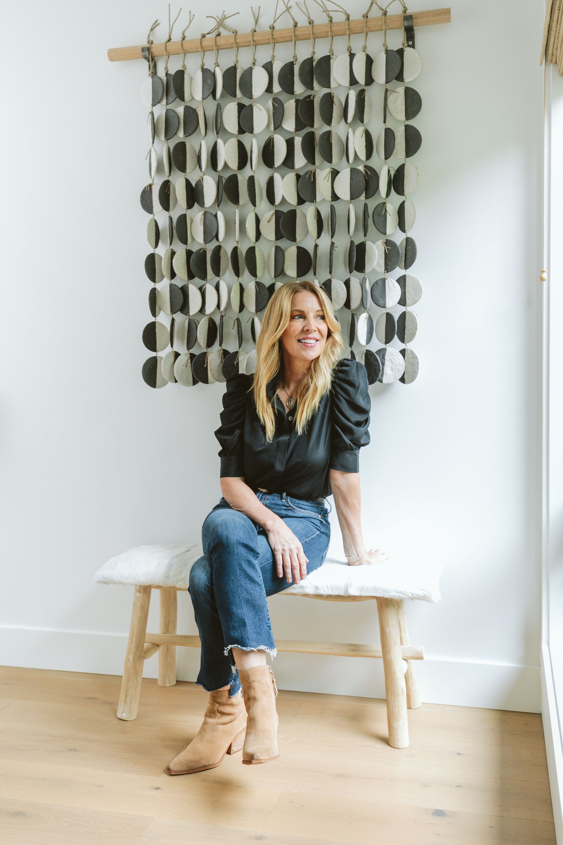 A woman is sitting on a bench in front of a wall hanging.