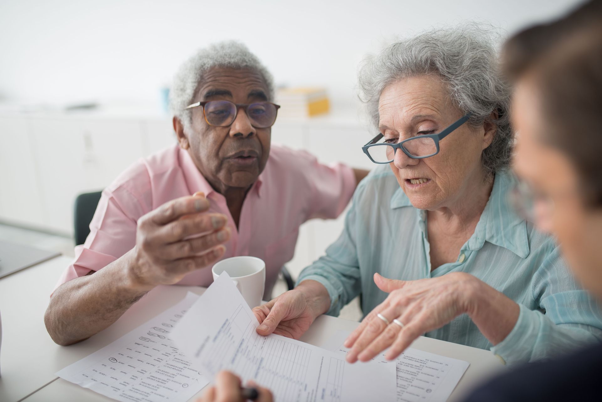 Two seniors reviewing papers together at a table, one pointing while the other reads with glasses.