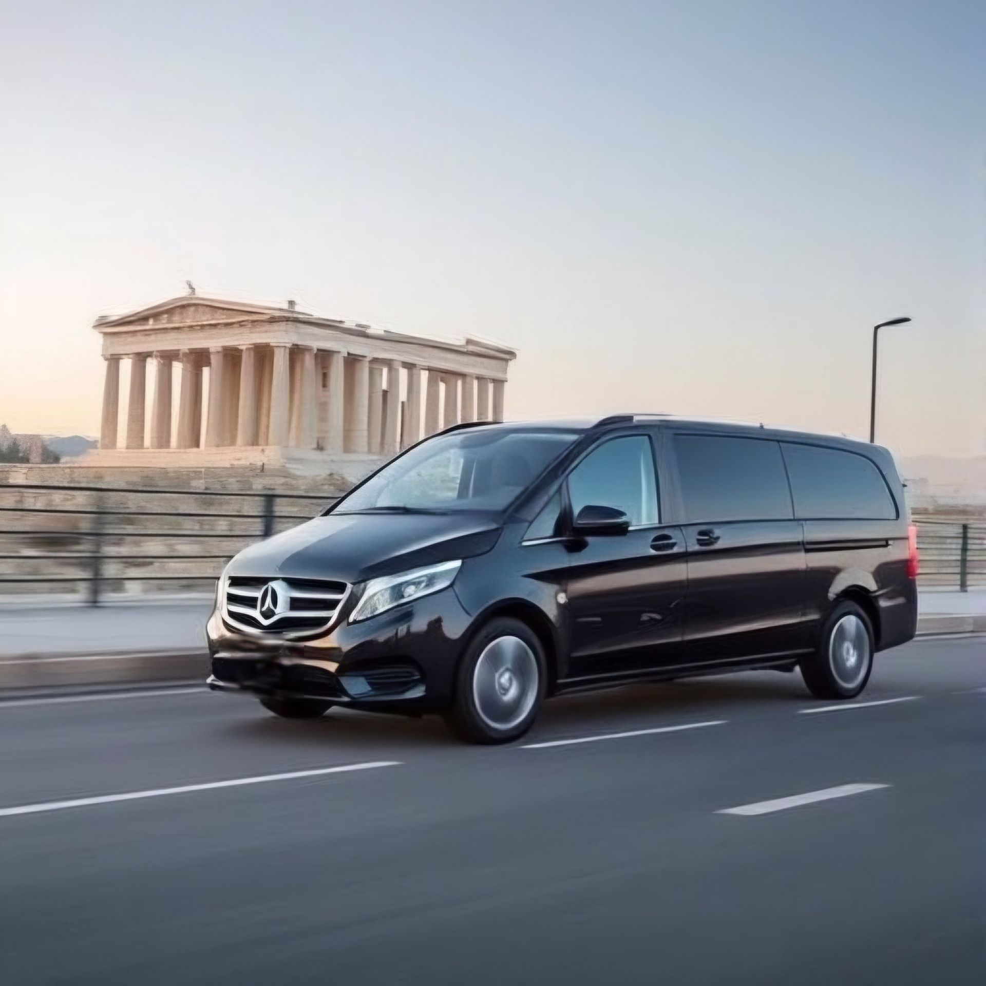 Modern vehicle parked outside a luxury hotel in Athens, ready for a hotel transfer service. A professional driver stands beside the vehicle, with the hotel entrance visible in the background, emphasizing the convenience and comfort of seamless transportation to and from Athens' hotels.