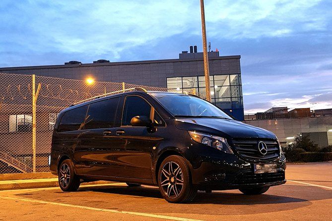 Minivan transfer from Athens Airport to Athens City, showing a spacious van and city landmarks for group travel comfort