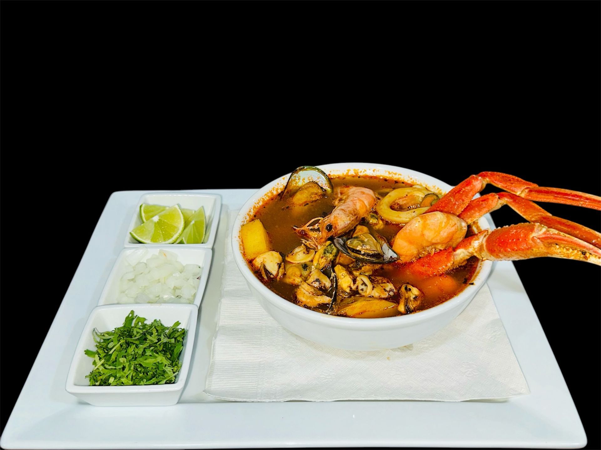 A bowl of seafood soup with crab legs on a white plate.