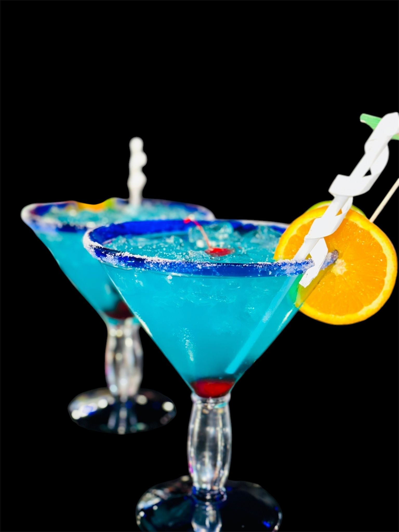 Two martini glasses filled with blue liquid and orange slices on a black background.