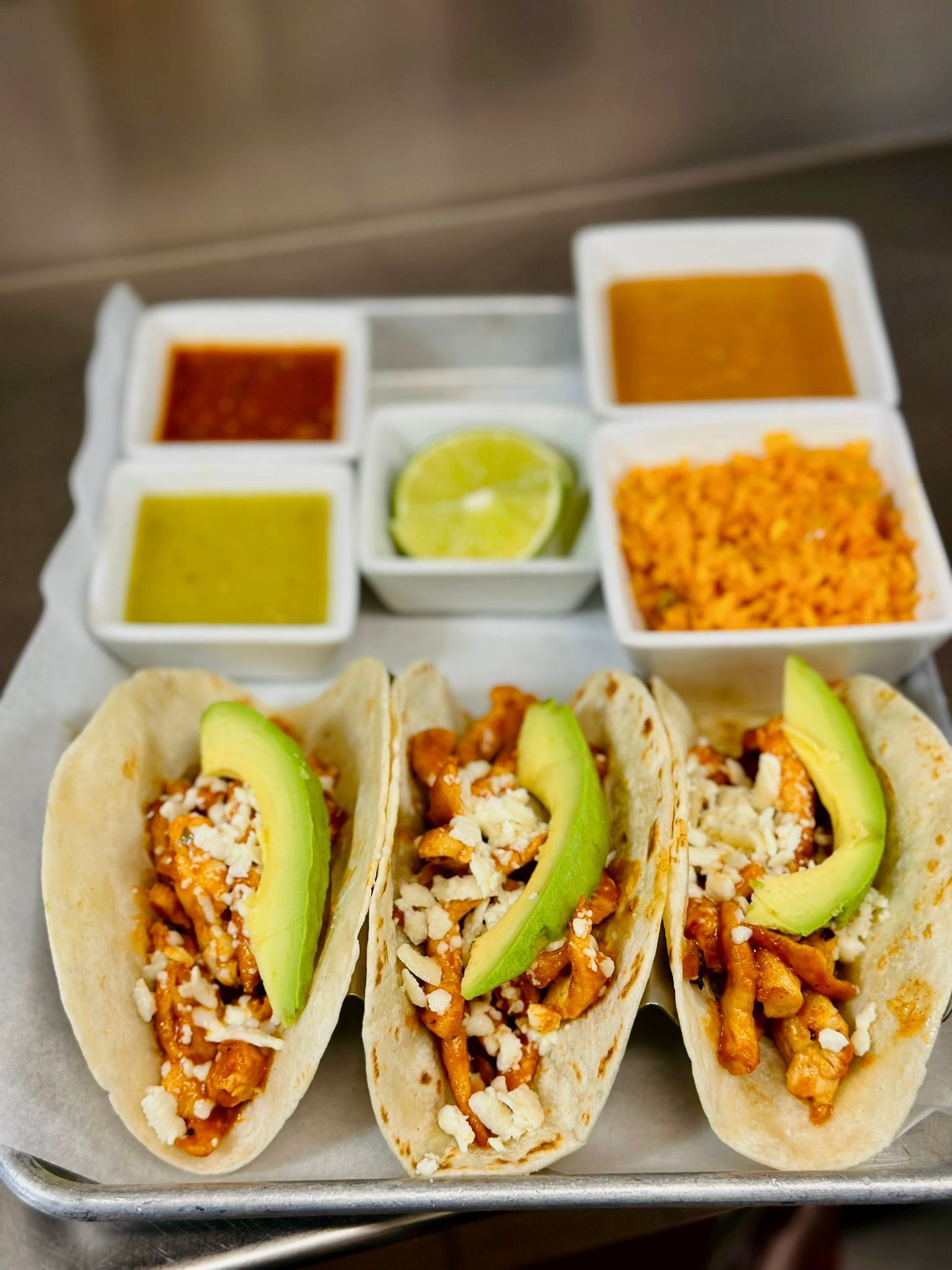 A tray of tacos with avocado , cheese and sauces on a table.