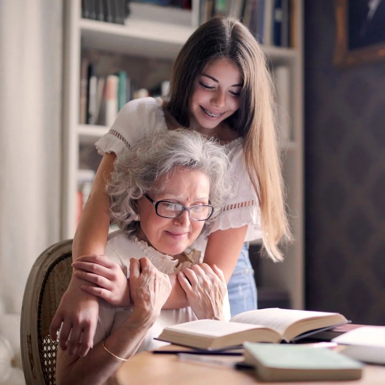 Woman and child smiling over an open book at a table in a cozy room