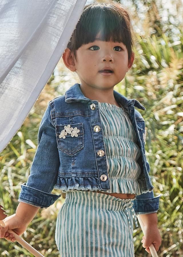 Bambino che indossa giacca di jeans, top a righe e pantaloni, all'aperto.