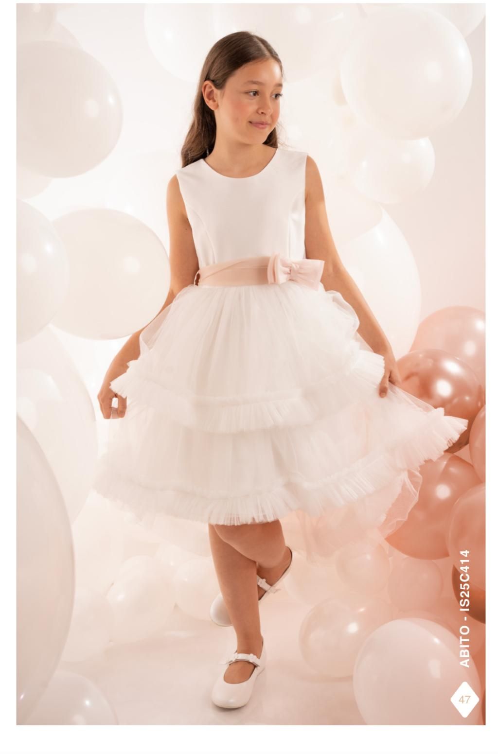 Ragazza con abito bianco e fascia rosa, circondata da palloncini.