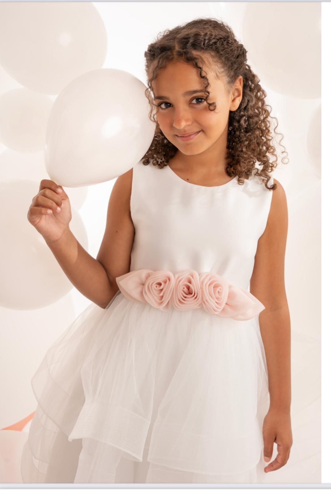 Ragazza con abito bianco e cintura floreale rosa che tiene in mano un palloncino.