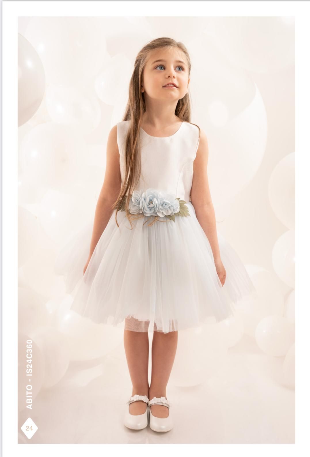 Ragazza con abito bianco e fascia di fiori blu, che guarda verso l'alto, circondata da palloncini.