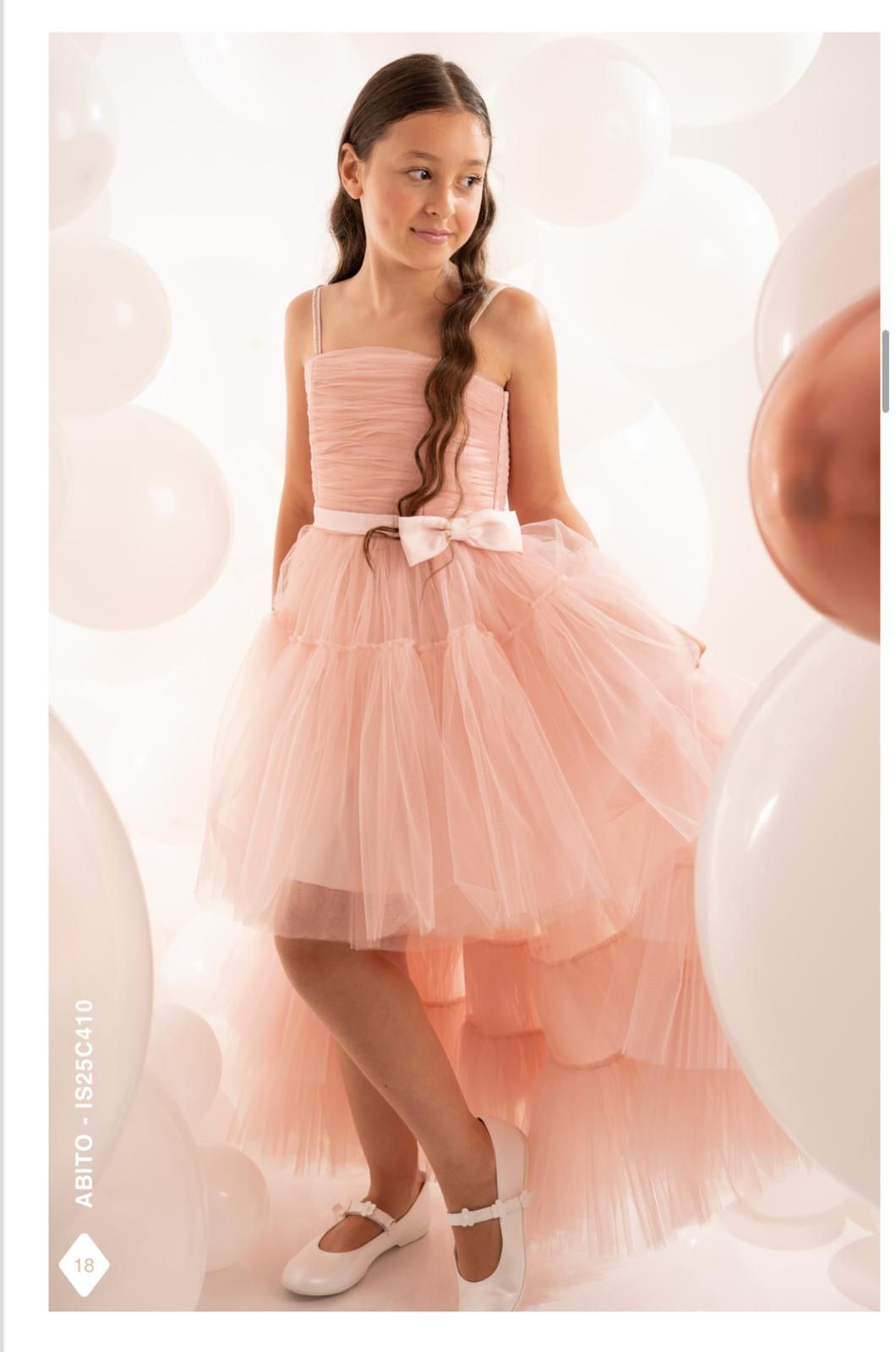 Ragazza con abito rosa e gonna di tulle, in piedi tra palloncini bianchi.