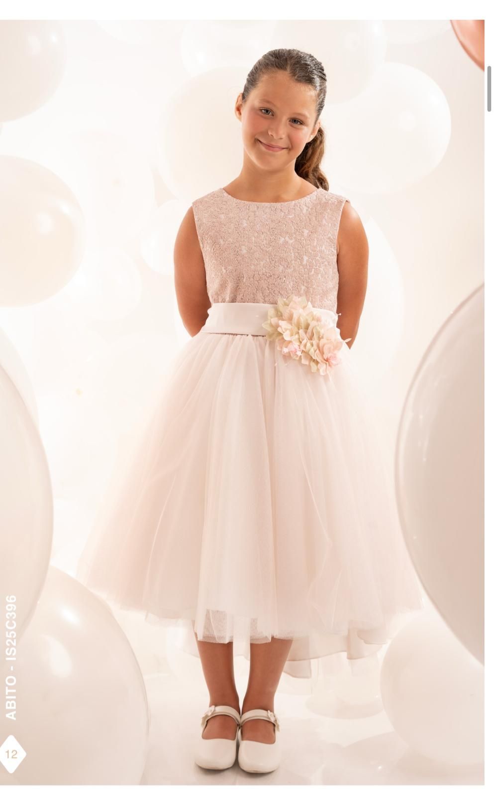 Una ragazza in abito formale rosa sorride e sta in piedi davanti a dei palloncini bianchi.