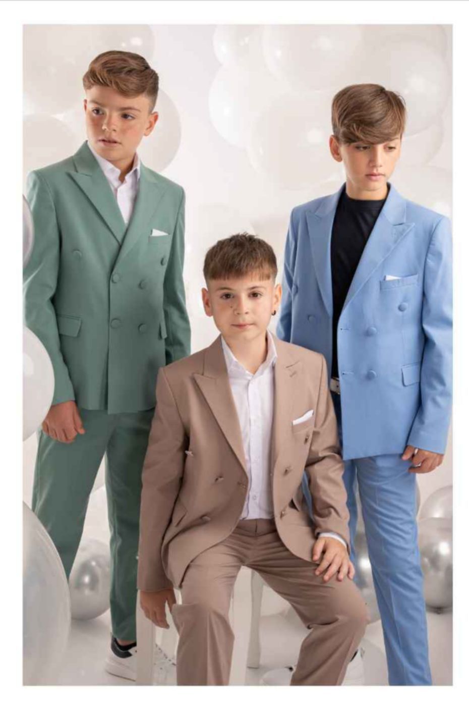 Tre giovani in giacca e cravatta posano davanti a uno sfondo di palloncini bianchi.