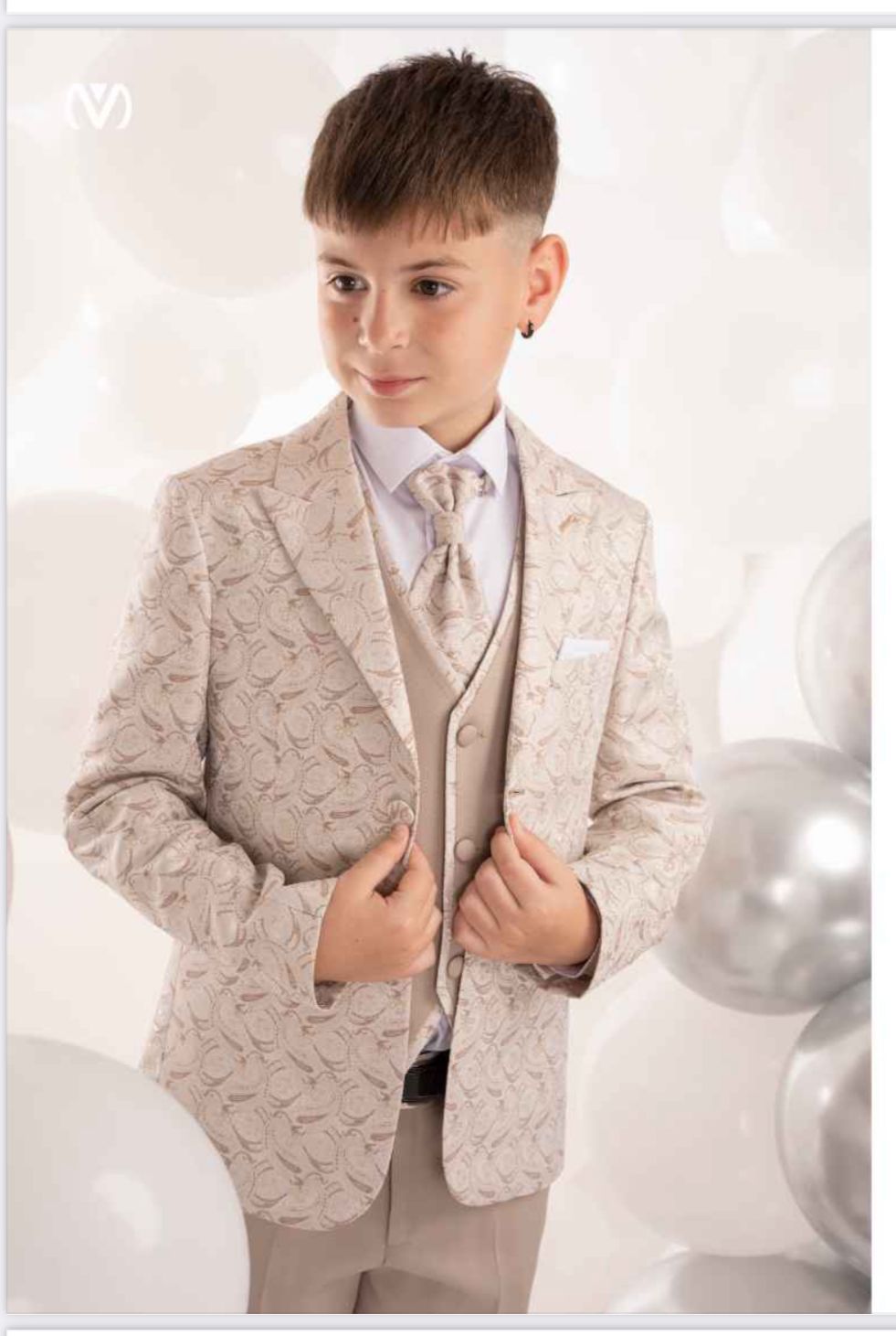 Ragazzo in abito beige e cravatta, sorridente, circondato da palloncini.