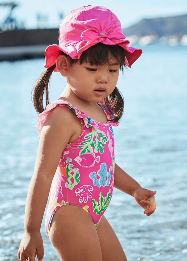 Ragazza in costume da bagno rosa e cappello che cammina su una spiaggia.