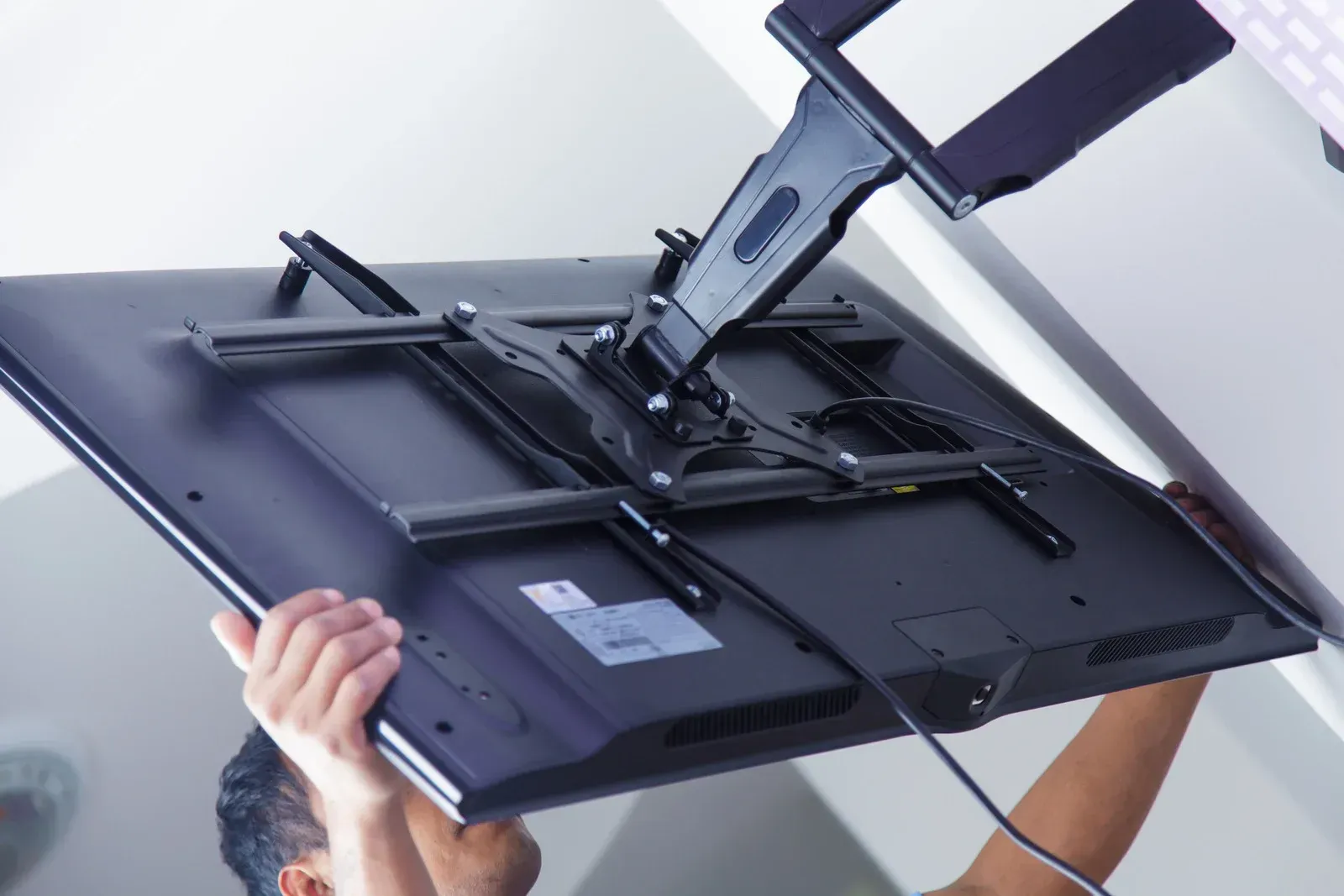 Person installing a TV on a wall mount, showing the back of the TV.