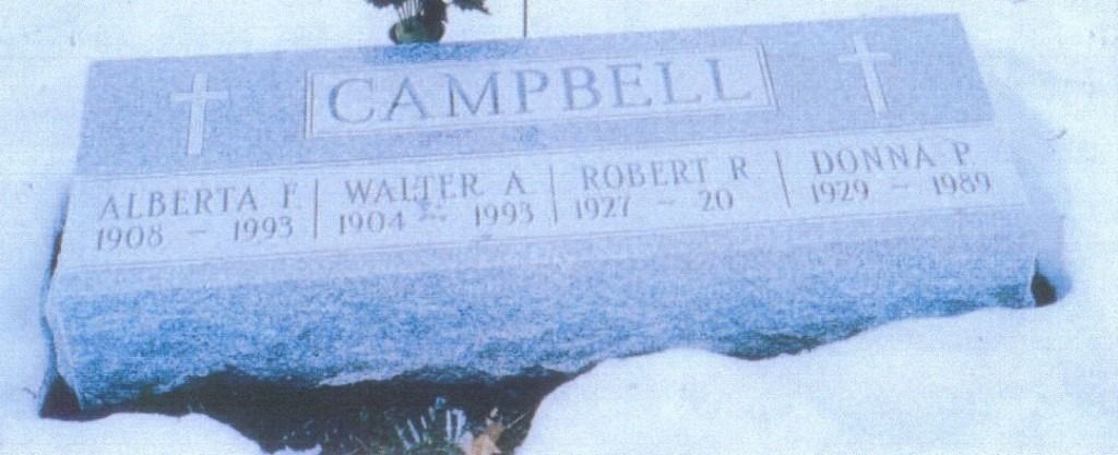 A snow-covered headstone in a cemetery reads 