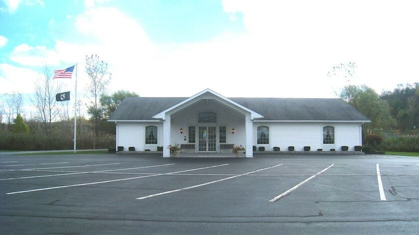 White building with flags, parking lot, and sky.
