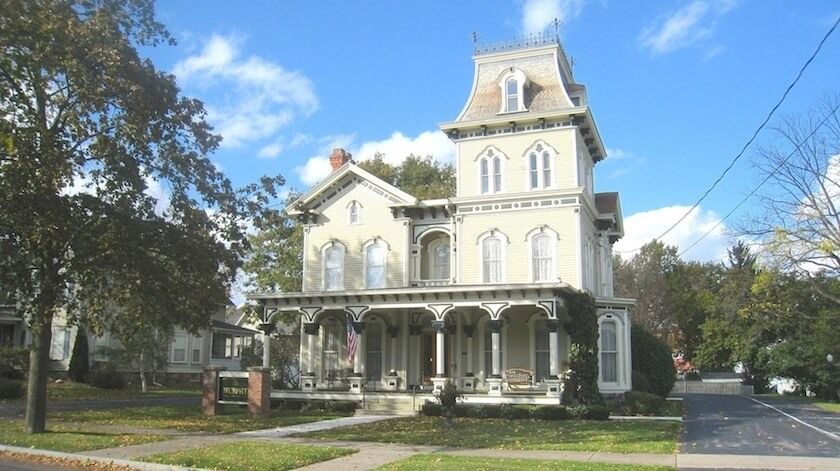 Large beige Victorian house with a tower, porch, and blue sky background.