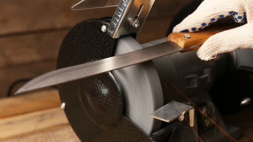 A person wearing a glove sharpens a knife on a bench grinder, close-up.