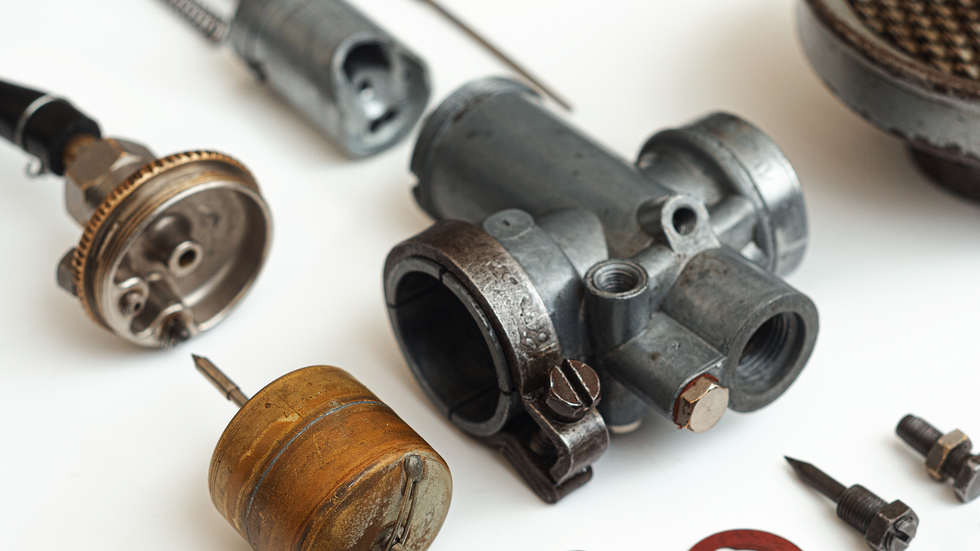 Disassembled motorcycle carburetor components on a white surface.