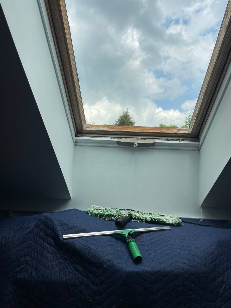 A green window cleaner is sitting on a blue blanket under a skylight