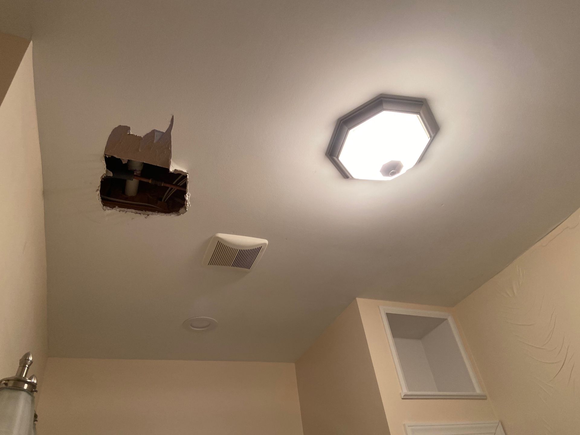 A bathroom with a hole in the ceiling and a light