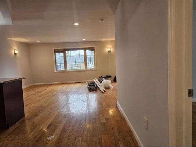 An empty living room with hardwood floors and a large window.