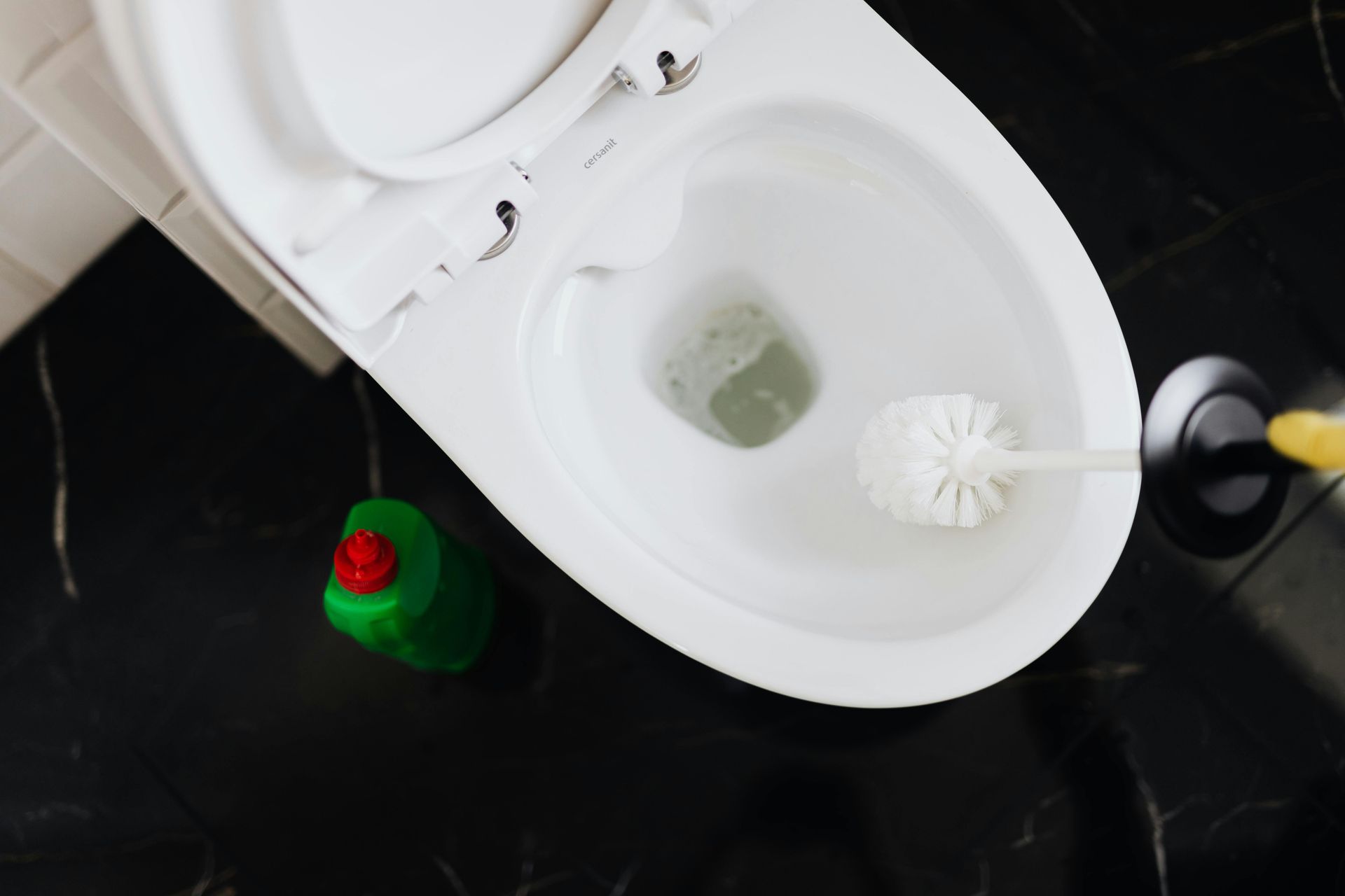 A toilet is being cleaned with a toilet brush