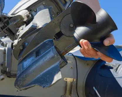 A person holding a black boat propeller next to a damaged outboard motor.